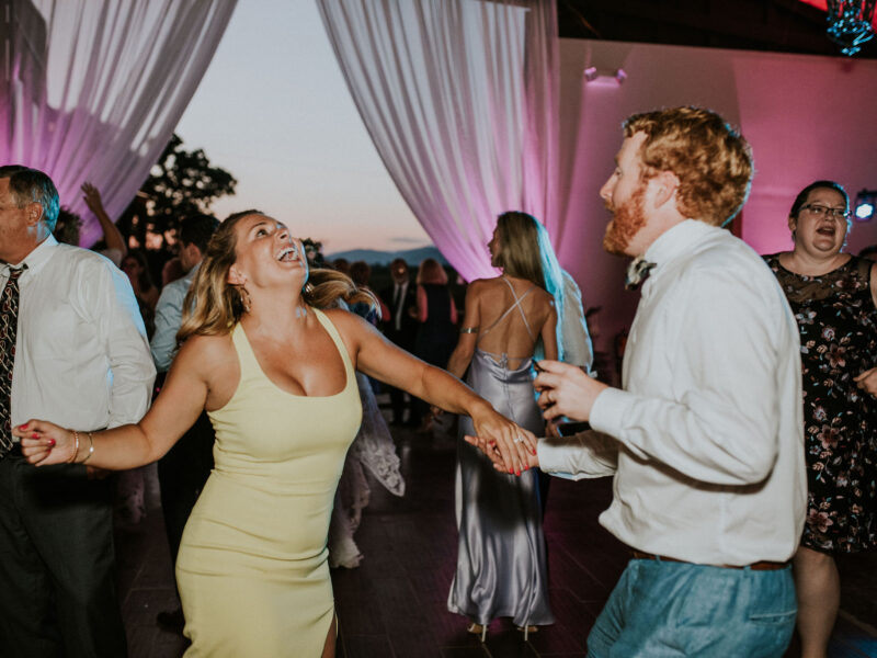 Guests dancing at White Oaks Barn with uplights around the dance floor and on the drapes